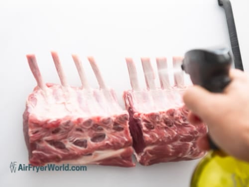 Lamb rack cut in half and being sprayed with oil