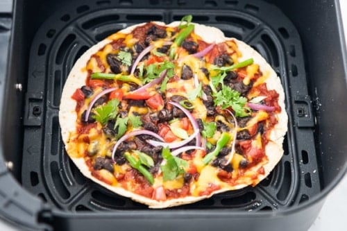 Tortilla in air fryer basket with pizza toppings