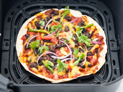 Tortilla in air fryer basket with pizza toppings
