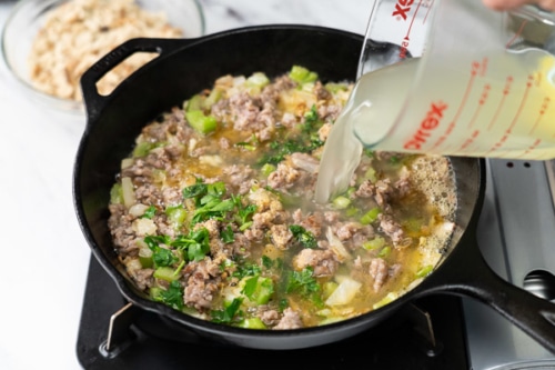 Broth being poured into skillet with onions, celery, and sausage