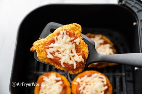 Cooked parmesan chicken in spatula above air fryer
